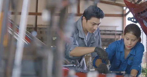 Mechanics instructor teaching female trainee to repairing a car in a garage Stock Footage 100229448