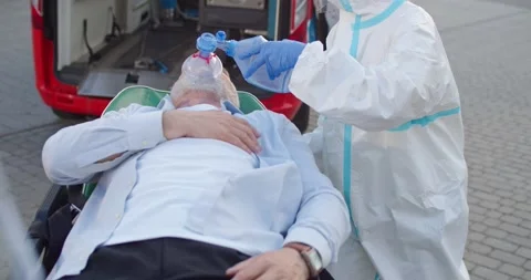 Medic in personal protective equipment taking old man in oxygen mask to the Stock Footage 158314686