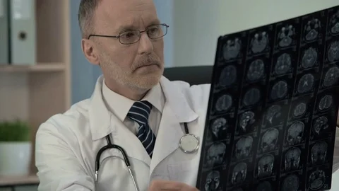 Medic studying MRI and making sure of serious disease writing mail to colleagues Stock-Footage 77740711