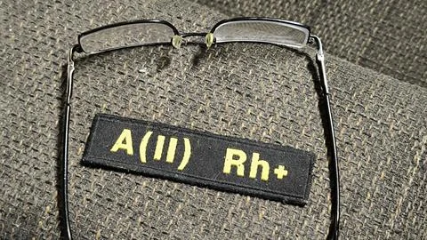 Medical blood type patch next to eyeglasses on a textured fabric surface. 写真素材