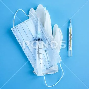Medical disposable syringe, ampoule, gloves, mask and thermometer on blue bac Stock Photos