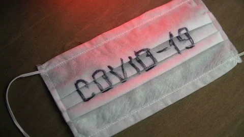 Medical mask with the inscription "COVID-19" on a dark background with red light Stock Footage