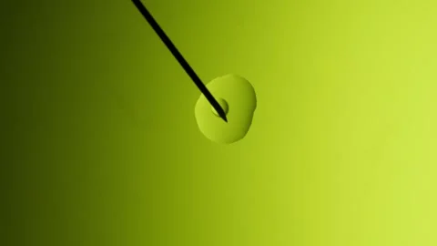 Medical needle makes drops of different sizes on a yellow gradient surface. Stockbeeldmateriaal 303060951