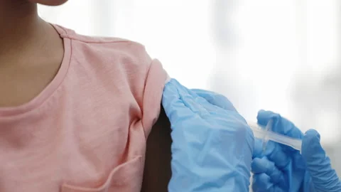 Medical nurse in safety gloves is making a vaccine injection to a kid patient in Stock Footage