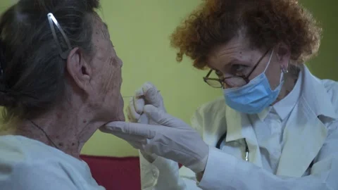 Medical professional in mask injects throat swab into sick elderly patient at Stock Footage