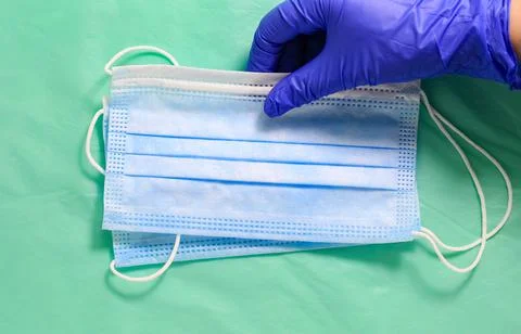 Medical protective masks in a stack, held by a hand in a protective glove. Stock Photos