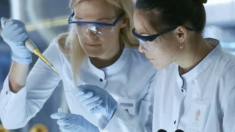 Medical Research Scientist Drops Sample on Slide and Her Colleague Examines it  Video stock 77950912