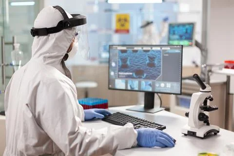 Medical scientist in ppe suit working with DNA scan image typing on pc. Stock Photos