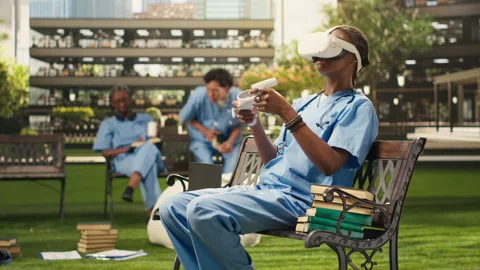 Medical student uses VR controllers and glasses in blue scrubs on bench Stock Footage 340961269