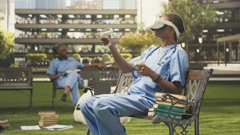 Medical student uses VR controllers and glasses in blue scrubs on bench Stock Photos