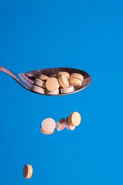 Medical tablets of round shape fall from a spoon on a blue background Stock Photos