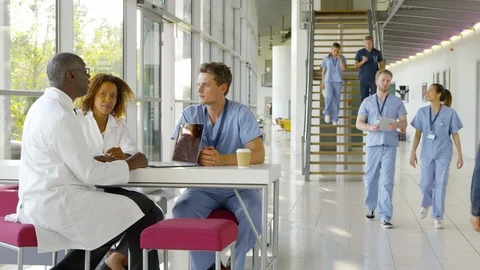 Medical Team Meeting Around Table In Busy Hospital Stock Footage