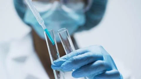 Medical worker adding few drops of blue liquid into test tubes, chemistry Stock Photos