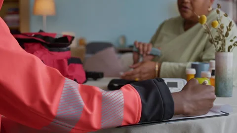 Medical Worker Filling Document while Providing Aid to Senior Patient at Home Stock Footage 318894254