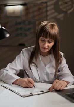 Medical worker writing notes in notebook working late in clinic office. female Stock Photos