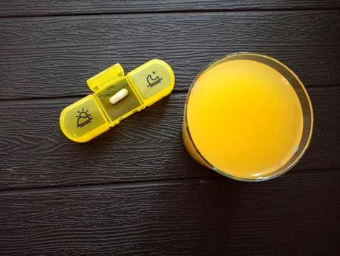 A medication container with an iron capsule and a glass of orange juice Stock Photos