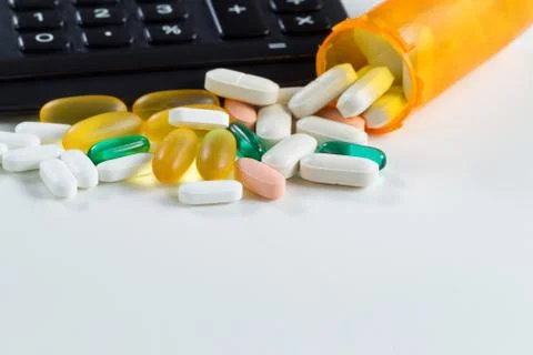 Medication pills with open bottle in front of calculator on white Stock Photos