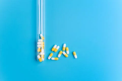 Medicine white and yellow pills or tablets drop out of the test tube on blue Stock Photos