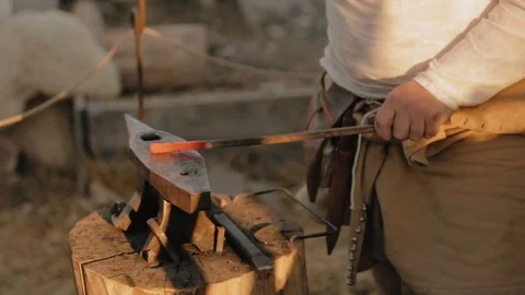 Medieval blacksmith with the beard wearing in straw hat beats hammer on the red Stock Footage 79997571