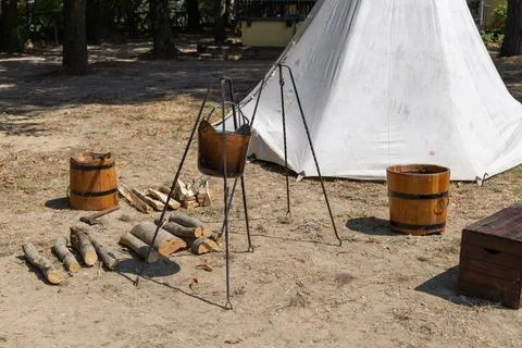 Medieval campsite setup with a tripod cauldron, wooden buckets, firewood, tent. Stockfoto's