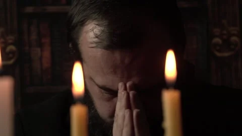Medieval Catholic Priest is Praying With Folded Hands in Front of Candles at Stock Footage 331412602