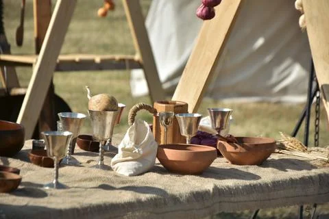Medieval feast table setting with silver cups, wooden mug and earthenware bowls Stock Photos