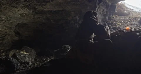 A medieval monk writes a book in a cave with a candle lit on a cold winter day Stock Footage 171474531