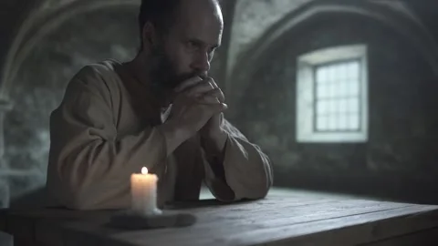 Medieval prisoner resting his chin on clasped hands and staring ahead Video stock 340079980
