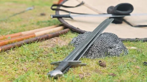 A medieval reenactment shows swords and chainmail laid on grass, surrounded by Stock Footage 345031904