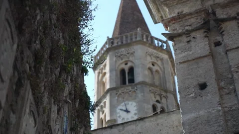 Medieval stone clock tower rises above narrow alley, framed by weathered 動画素材 347294353