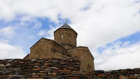 Medieval stone dome of Gergeti Trinity Church behind rocky wall  Stock Photos
