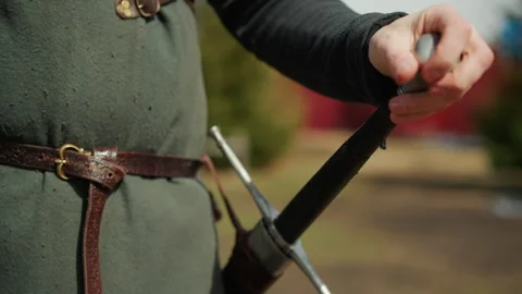 Medieval sword drawn by hand in outdoor reenactment, wool tunic and leather belt Stock Footage 345663603