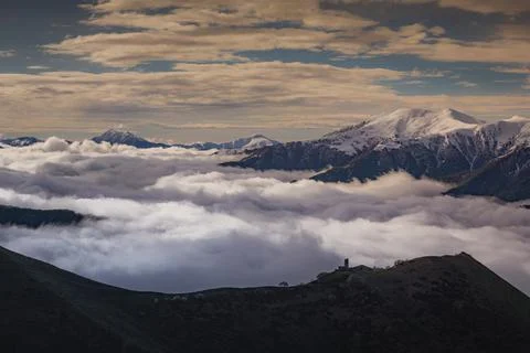Medieval tower on mount  above clouds, with snowy peaks in the background Stock Photos