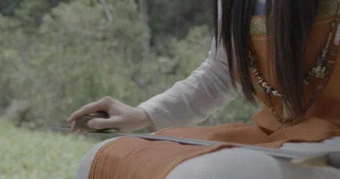 Medieval Women's Hand Sharpens Sword Blade with a Rock in the Forest Stock Footage 259392437