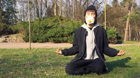 Meditating while deasises air pollution or pandemic in park in respiratory mask Stock Footage 129942747