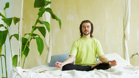Meditative man concetrating using yoga and sitting in asana in bed Stock Footage 141455070