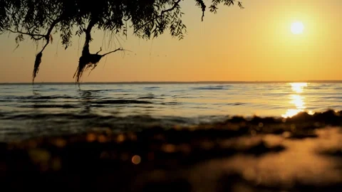 Meditative shot of the setting summer sun, calm waves on the sandy shore and Stock Footage 255073775