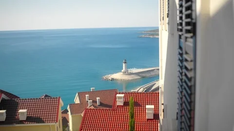 Mediterranean town rooftops and lighthouse on a rocky breakwater Stock Footage 327013701