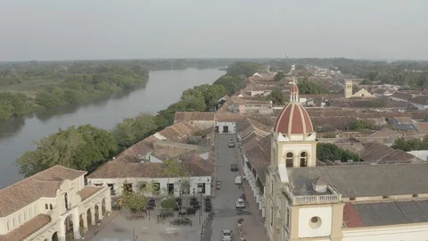 Medium aerial sails down shoreline of Magdalena river in Mompox, Colombia Видео 108571445