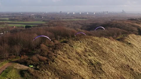 Medium aerial shot of three paragliders skimming along the crest of a grassy Stock Footage 300665934
