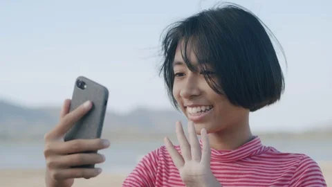 Medium close up of Asian girl using smartphone video call or chat on the beach Stock Footage 126129840