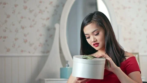 Medium close-up impressed beautiful Asian woman opening gift box and smiling at Stock Footage 99492142