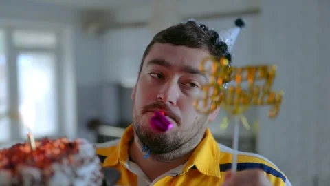 Medium Close Up One Man Holding Birthday Cake Blowing Party Horn Video stock 334042723