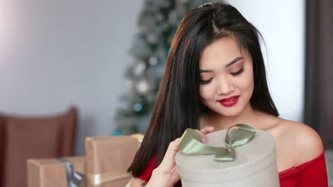 Medium close-up portrait of curious young Asian woman opening Christmas gift box Vídeos de archivo 99490263