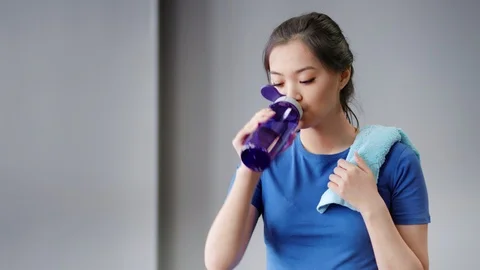 Medium close-up portrait of smiling Asian woman tired after workout drinking Stock Footage 97851718
