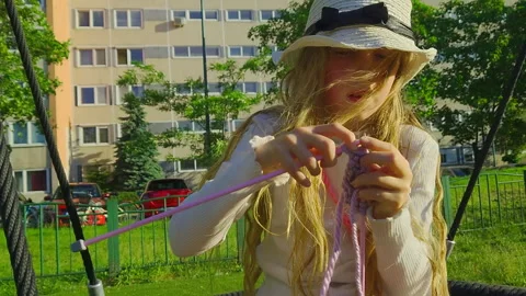 Medium Close Up Shot of Girl Knitting Purple Yarn on Playground Swing in Video stock 335351401
