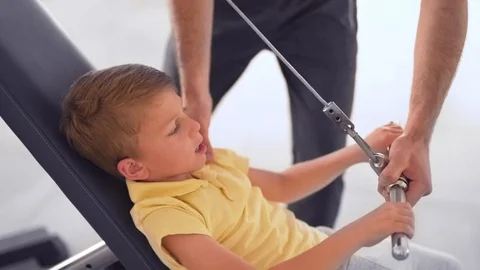 Medium close-up shot of a young boy exercising on a pulling machine in the Stock Footage 115504999