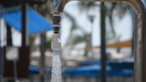 Medium close up standing under an outside swimming pool shower under a clear blu Vidéo 95025511