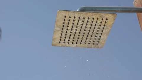 Medium close up standing under an outside swimming pool shower under a clear blu Видео 96852987