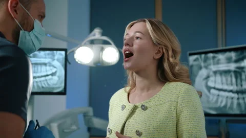 Medium close up of young blonde explaining dental problems to male dentist Stock Footage 258104285